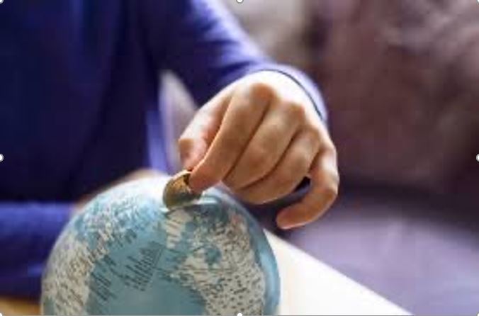 Hand putting money in piggy bank shaped like a globe